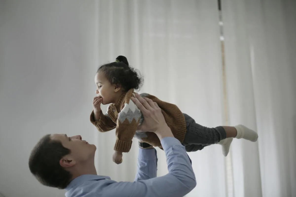 Padre levantando a una niña pequeña en casa, representando asuntos de manutención infantil en Maryland.