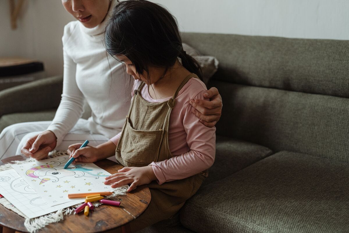 Caregiver sitting with a young child coloring at home, representing family stability and SIJS custody guidance for Maryland families